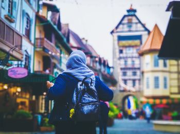 Rear view of man standing on street against buildings in city