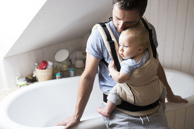 Father with baby in baby carrier in bathroom