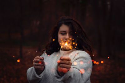 Portrait of young woman holding illuminated lighting equipment at night