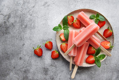 Homemade frozen strawberry ice cream popsicles and fresh strawberries on a concrete background. 