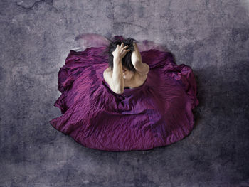 High angle view of depressed woman with hands in hair wearing purple dress while sitting on floor