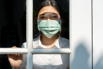 Portrait of woman wearing mask seen through window