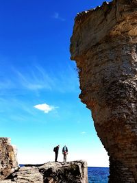 People standing on cliff against blue sky