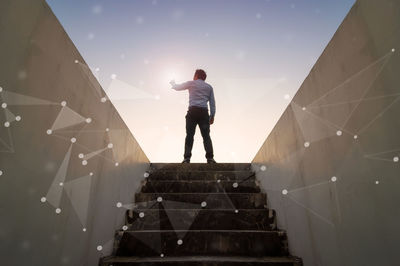 Rear view of man standing on staircase against sky
