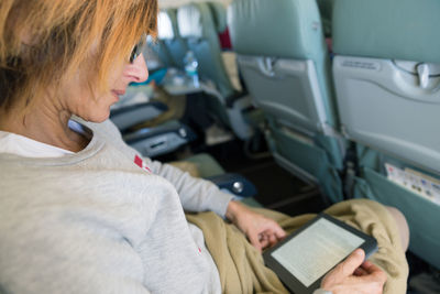 Woman reading book in digital tablet in airplane