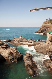 Distant view of people enjoying on rocks by sea against clear sky