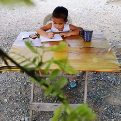 Girl writing in book while sitting outdoors