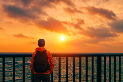 Man standing by railing against sea during sunset