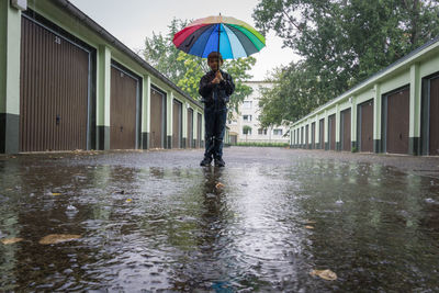 Full length of boy standing with umbrella amidst garage during rain