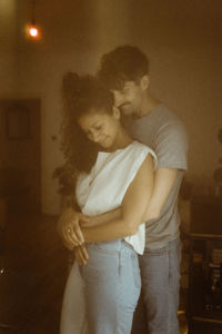 Boyfriend embracing girlfriend from behind while standing at home