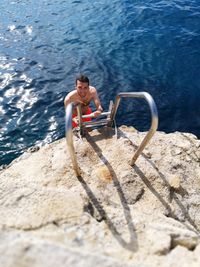 High angle view of shirtless man climbing ladder against sea