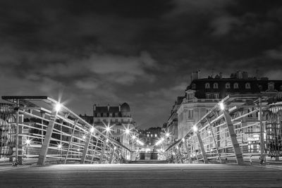 Illuminated road against cloudy sky at night