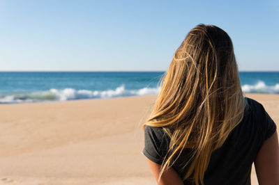 Rear view of woman standing on beach against clear sky