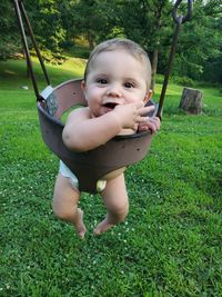 Portrait of cute boy sitting on swing over grass