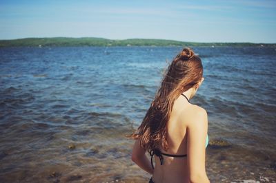 Young woman in bikini standing at beach against sky