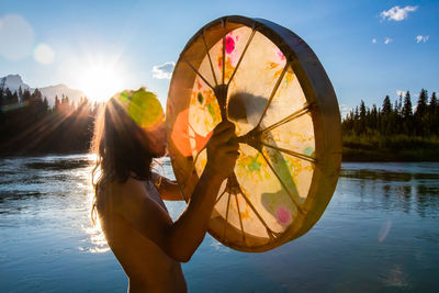 Side view of woman standing by lake against sky