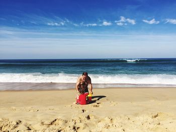 Father with daughter on shore at beach against sky