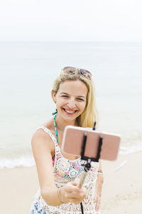 Cheerful woman taking selfie while standing at beach