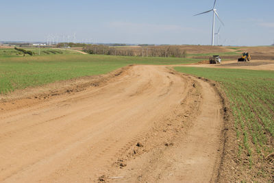 Dirt road amidst agricultural field against sky