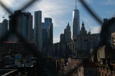 Buildings in city seen through chain link fence