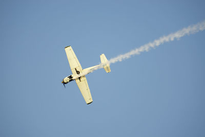 Directly below shot of airplane leaving smoke while flying in clear blue sky