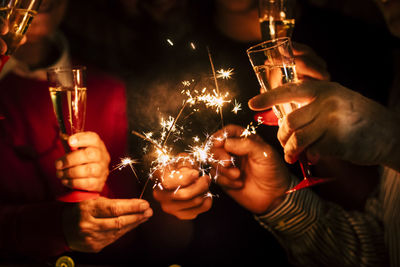 Midsection of friends holding sparklers and champagne at night