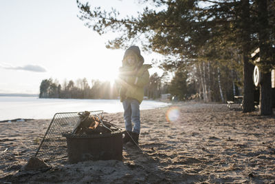 Young boy stood next to a fire on the beach in sweden