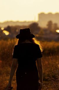 Rear view of silhouette woman photographing against sky during sunset