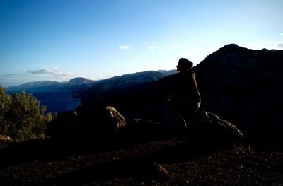 Woman sitting on rock at mountain peak against blue sky