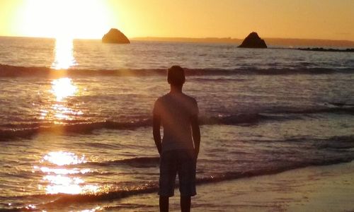 Rear view of silhouette man standing at beach during sunset