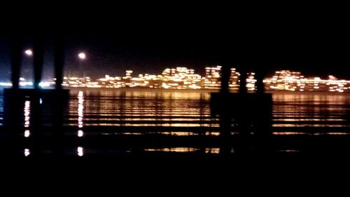 Illuminated city by river against clear sky at night