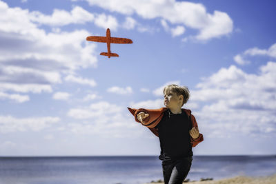 Little caucasian blond boy launching red toy plane in front of blue sly