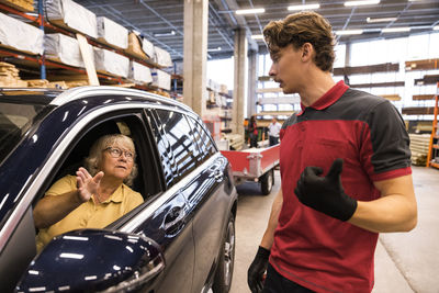 Salesman guiding direction to female customer sitting in car at hardware store