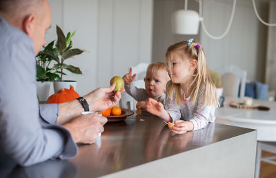 Grandfather giving fruit to children at home