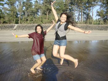 Portrait of happy friends jumping at beach against trees