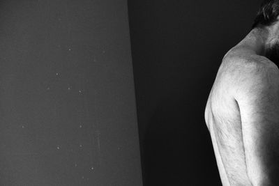 Low section of shirtless man standing against wall