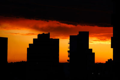 Silhouette buildings against dramatic sky during sunset