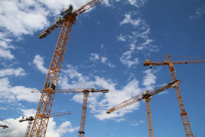 Low angle view of cranes at construction site against sky