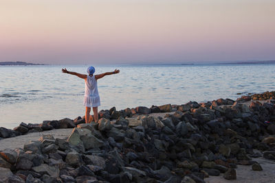 Rear view of woman standing on rocks by sea against sky