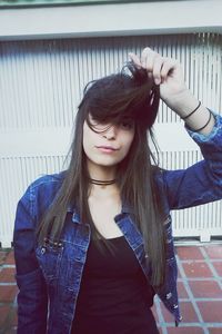 Portrait of young woman with hand in hair standing against wall