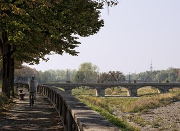 Rear of man cycling on footpath against view of bridge