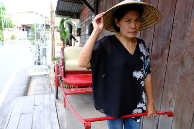 Mature woman wearing asian style conical hat while pulling rickshaw in city