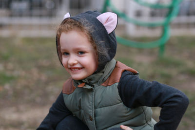 Smiling girl in warm clothing looking away while crouching at park