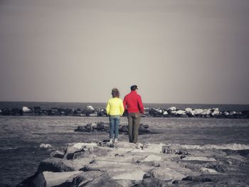 Rear view of men standing on beach against clear sky