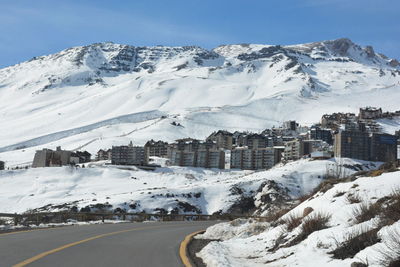 Snow covered road by buildings against sky