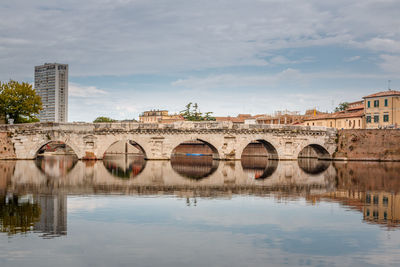 Arch bridge over river by buildings against sky