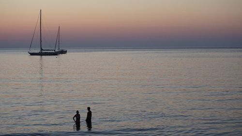 Silhouette people on sea against sky during sunset