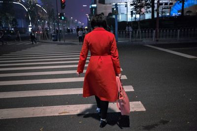 Rear view full length of woman crossing road in city at night