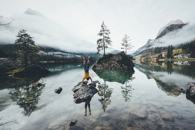 Scenic view of lake against sky during winter with man doing handstand in foreground