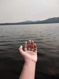 Cropped hand of person over lake against clear sky